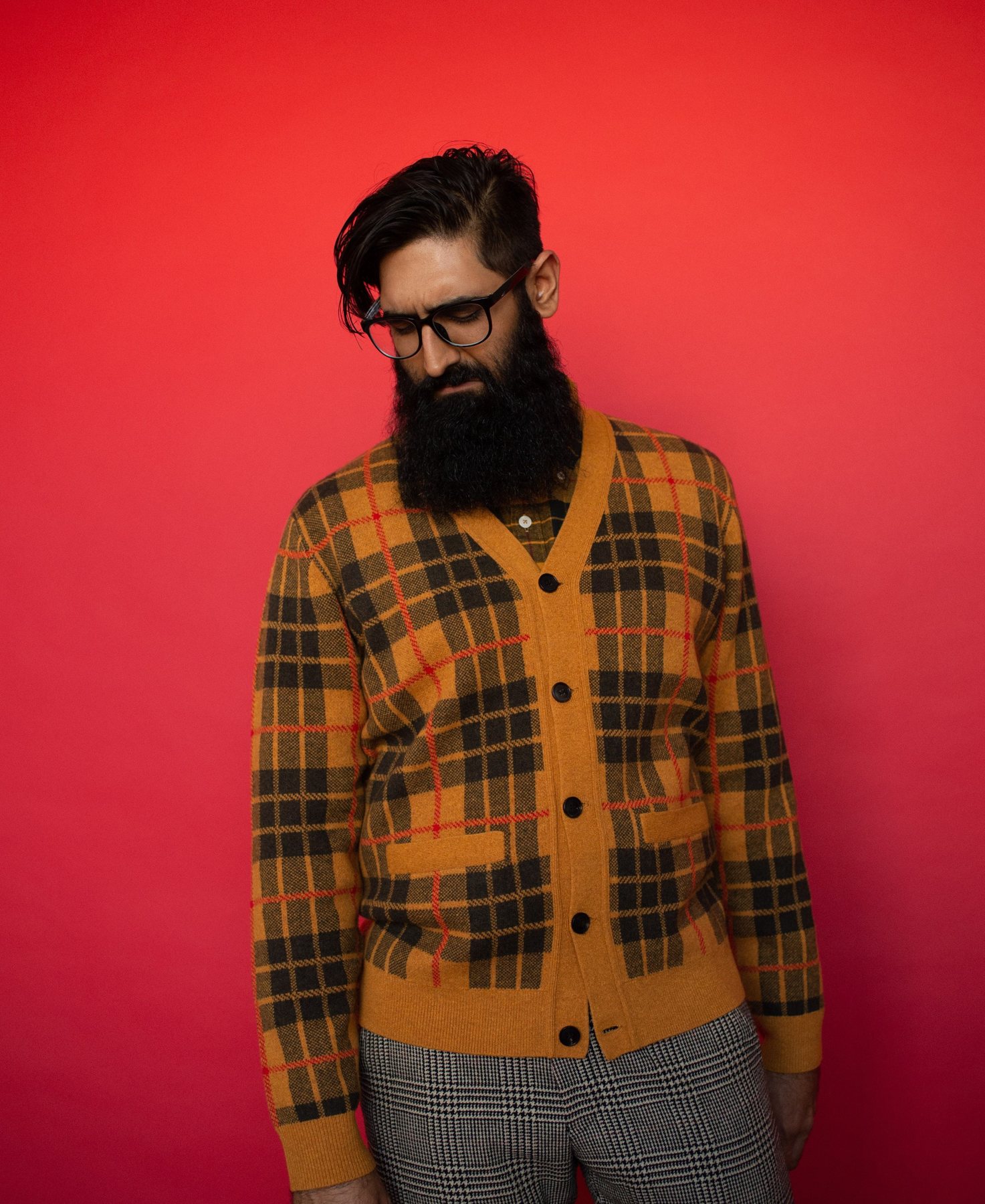 Portrait of Manan Pandya in a plaid cardigan against a red wall